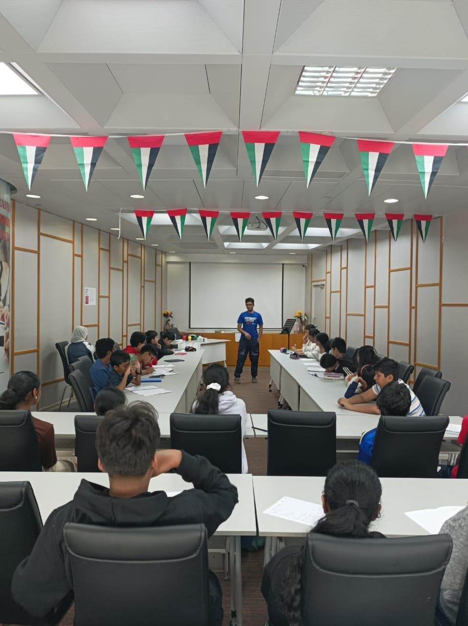 A full club meeting under UAE flag bunting, with a member speaking at the front
